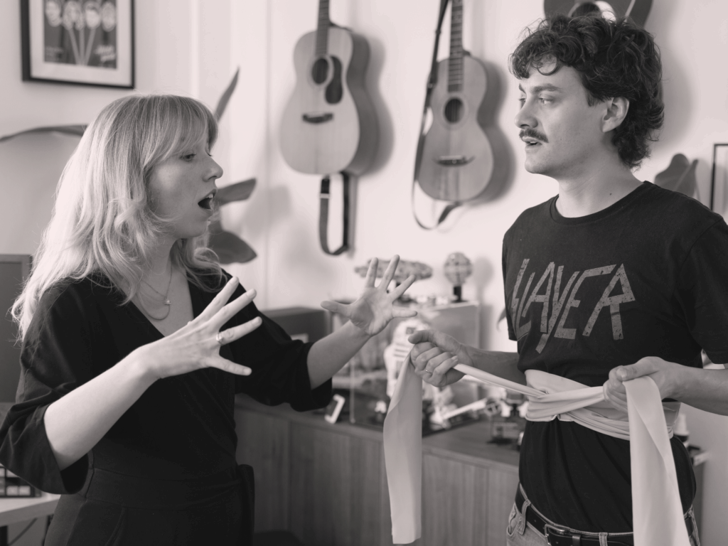 Stimmbildung und Gesangsunterricht – Lehrerin erklärt Gesangstechnik im Musikraum mit Gitarren.