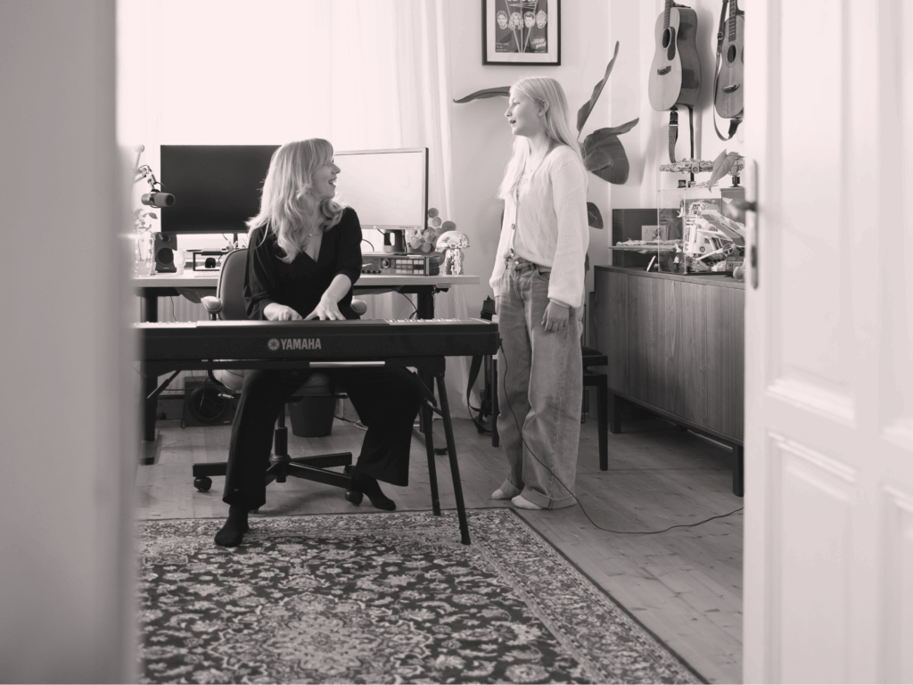 Gesangsunterricht Linz – Student:in arbeitet am Tisch, Lehrerin begleitet beim Stimmtraining.